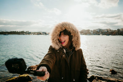 Happy woman taking selfie with camera while standing against lake