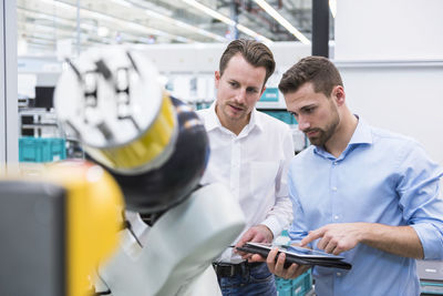 Two men with tablet examining assembly robot in factory shop floor