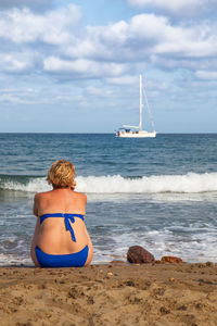 Rear view of woman sitting on shore against sky