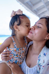 Young mother laughing with a funny face while her daughter embraces her neck and kisses cheek 