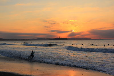 Silhouette man wading in sea against sky during sunset