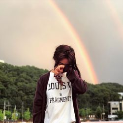 Full length of young woman standing against rainbow in sky