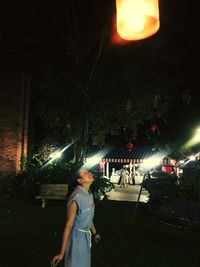 Woman standing by illuminated tree against sky at night