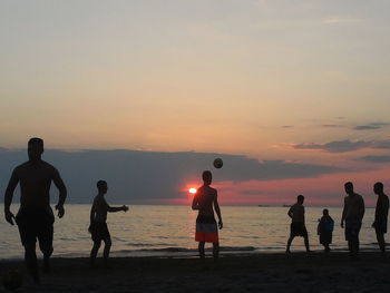 Silhouette people playing with ball on beach against sky during sunset