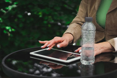 Hands of a young caucasian woman typing on the black screen of the tablet while sitting at a table