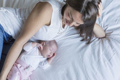 Directly above shot of smiling woman lying by sleeping daughter on bed at home