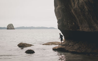 Man standing on cliff by sea against clear sky