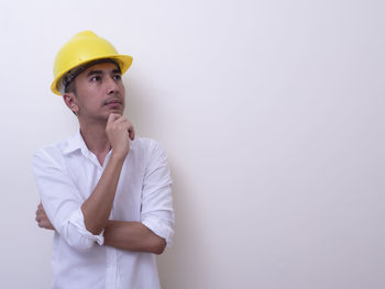 Young man looking away while standing against white wall