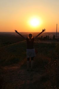 Rear view of woman standing on field against sky during sunset