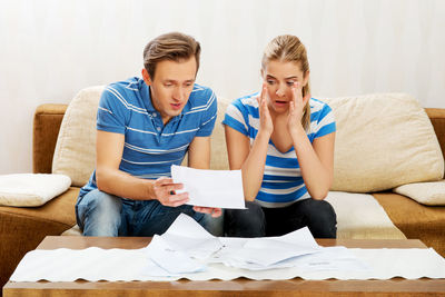 Tensed couple looking at document while sitting in home