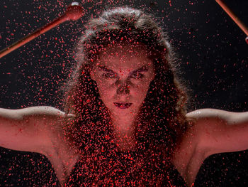 Close-up portrait of young woman seen through red liquid splashing against black background