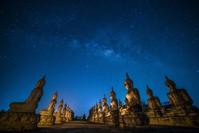 Low angle view of buddha statues against star field at night