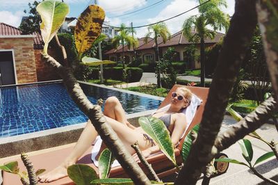 Full length of woman resting on lounge chair at poolside during sunny day