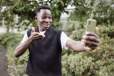 Young african man taking selfie or vlogging on phone in park, smiling