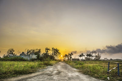 Road amidst field against sky during sunset
