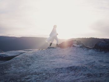 Woman in white clothes walking in sunlight in snowcapped mountains