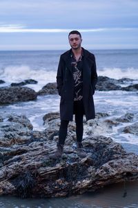 Portrait of young man standing on rock at beach