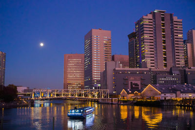 Illuminated buildings by river against sky at night