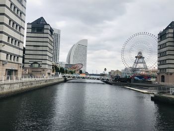 Bridge over river by buildings in city against sky