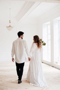 Rear view of couple holding hands while walking in room during wedding ceremony