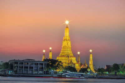 Illuminated building by street against sky during sunset