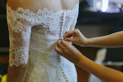 Cropped hands of woman buttoning bride dress