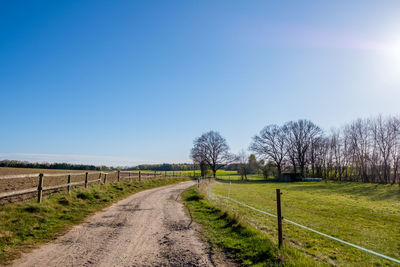 Dirt road amidst field against clear sky