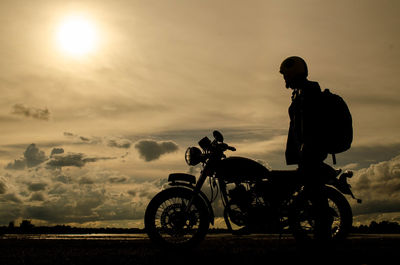 Silhouette man standing by motorcycle against sky during sunset
