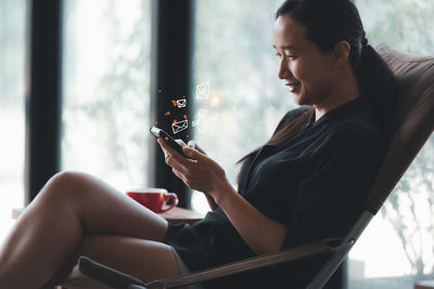 Woman using mobile phone while sitting on window