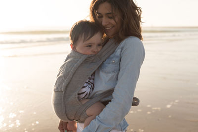 Mother carrying son in baby carrier while standing at beach