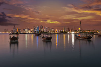 Illuminated boats in sea against sky during sunset