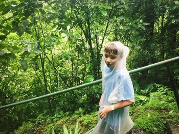 High angle portrait of boy wearing raincoat walking by railing in forest
