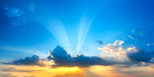 Low angle view of sunlight streaming through clouds during sunset