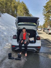 A young man on the back of a car wearing his snow boots