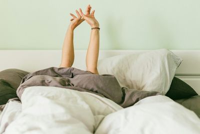 Woman with arms raised while relaxing on bed at home