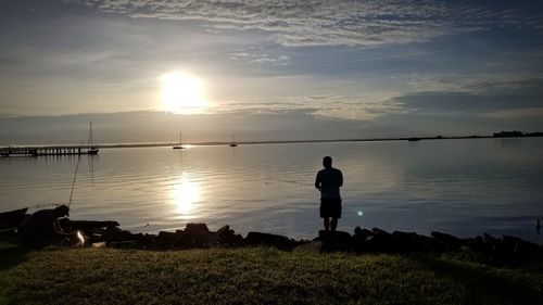 Silhouette man standing by lake against sky during sunset