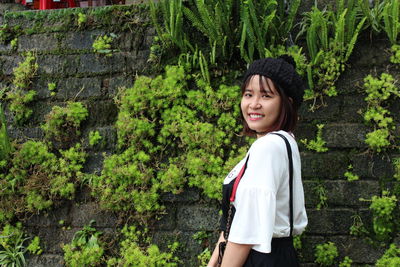 Portrait of smiling young woman standing against plants