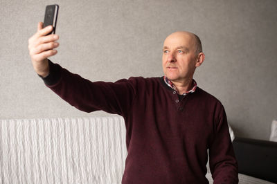 An adult man takes a selfie on his phone in the living room
