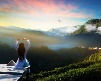 Rear view of woman sitting against mountains and lake