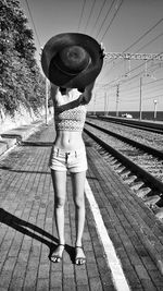 Woman holding hat while standing at railroad station platform