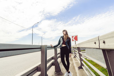 Relaxed young woman standing on bridge against cloudy sky