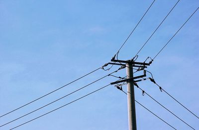 Low angle view of electricity pylon against blue sky