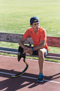 Young athlete with prosthetic leg sitting on bench at running track