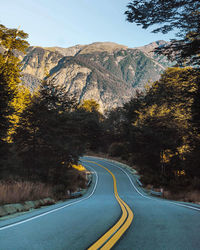 Country road amidst trees and mountains against sky