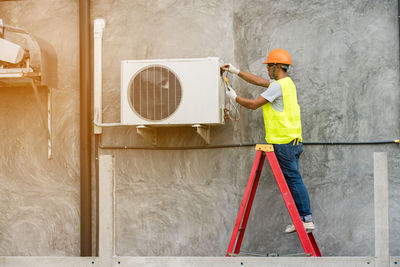 Side view of man repairing air conditioner