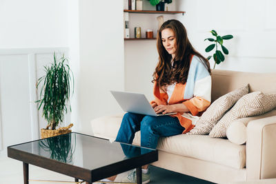 Young modern business woman sitting at home on the sofa uses a laptop for remote work.