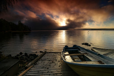 Boats moored at beach against cloudy sky during sunset