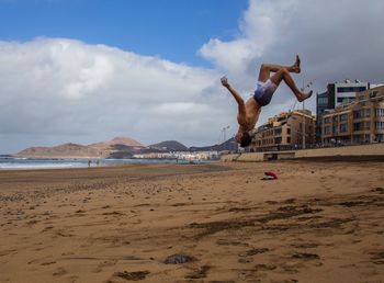 Man jumping at beach against sky