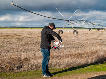 Man holding drone while standing on field against sky