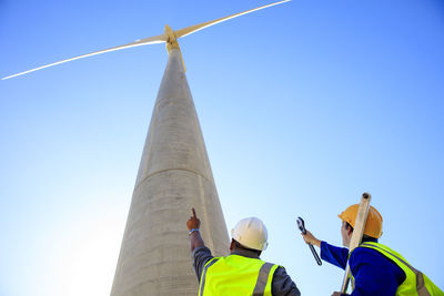 Low angle view of technicians in front of wind turbine